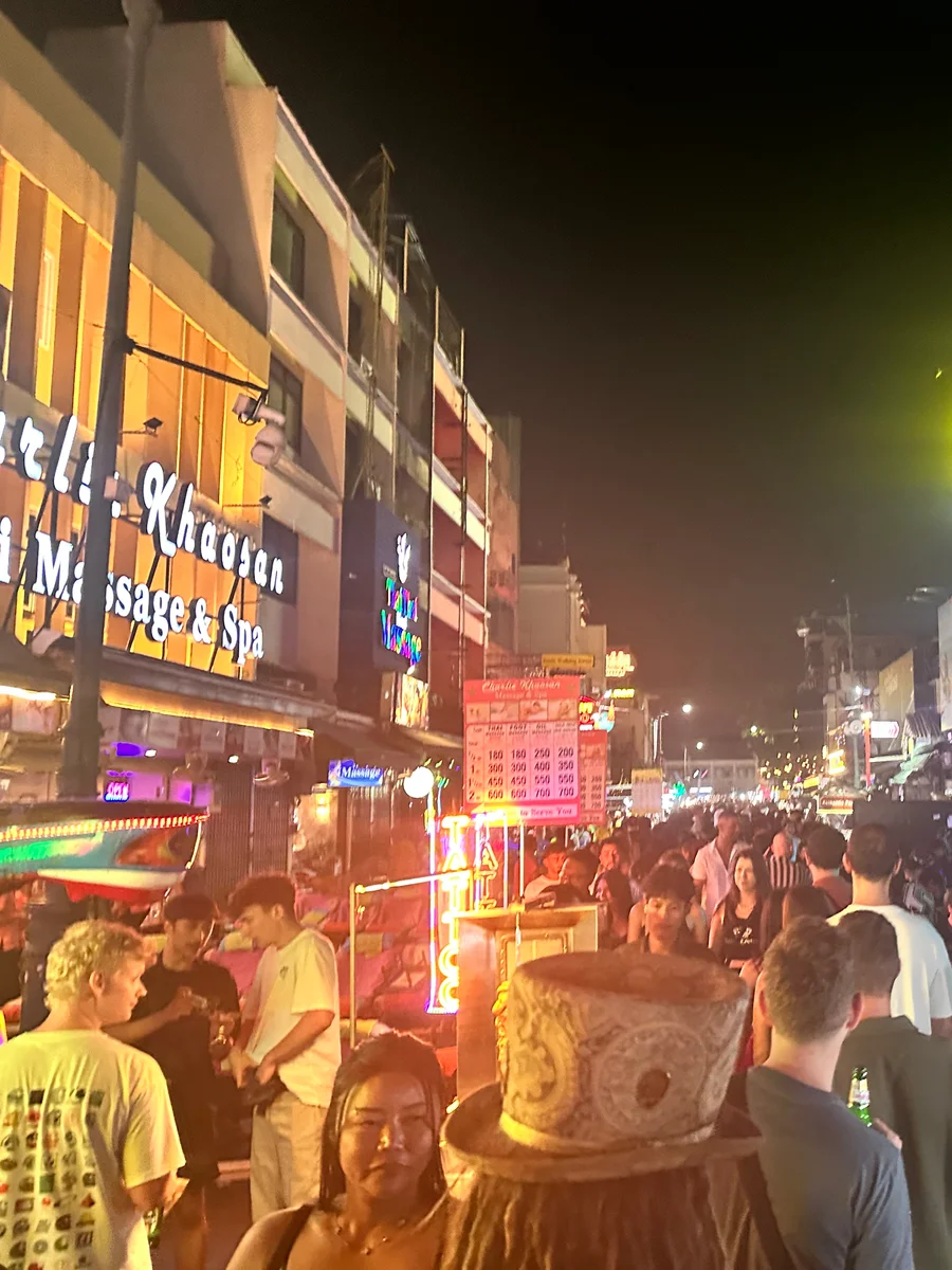 Bangkok night market or Chinatown street — neon, steam, stacked plastic stools