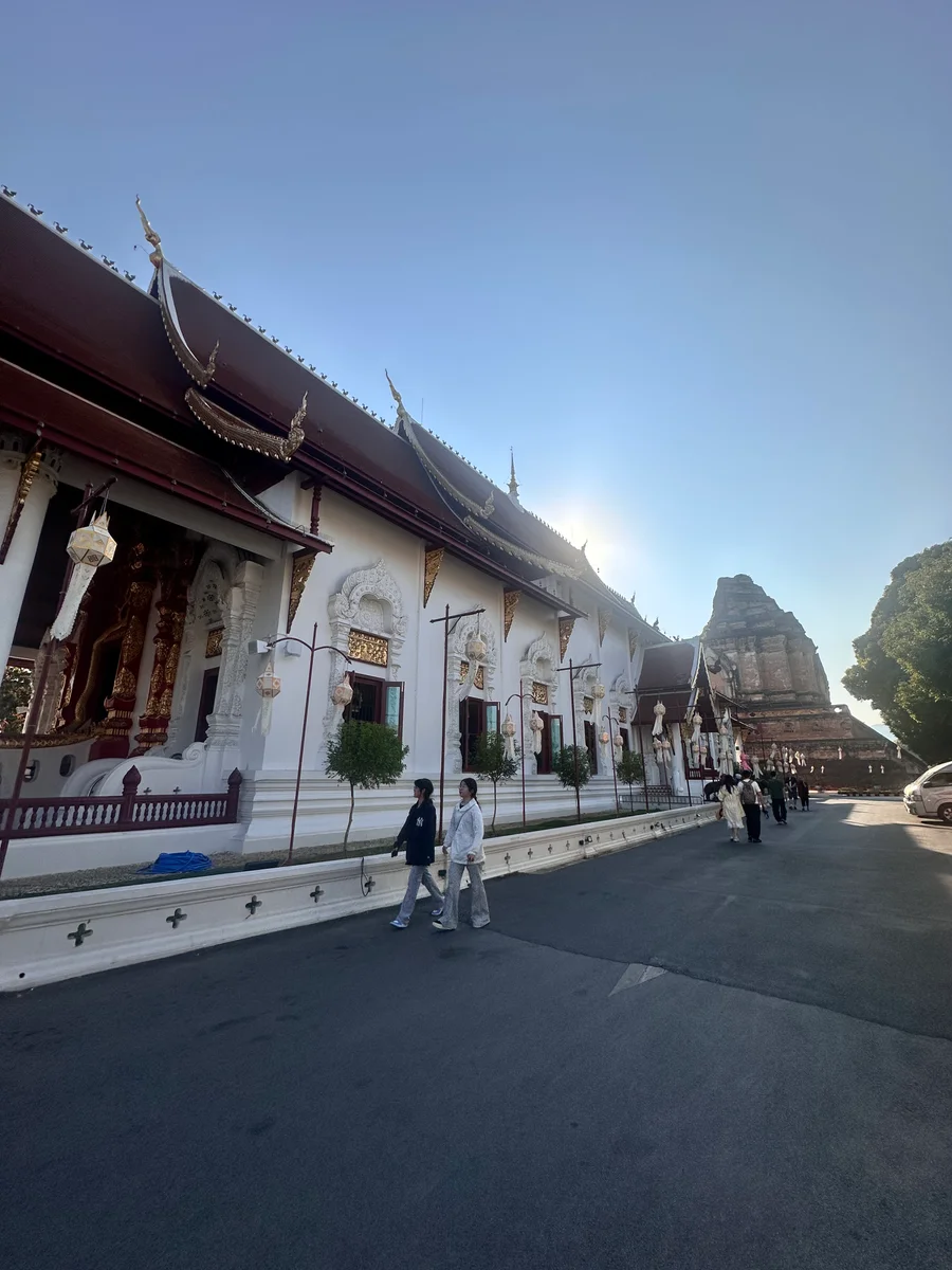 Wat Chedi Luang in Chiang Mai, late afternoon — visitors walking past the white viharn, the chedi ruins behind