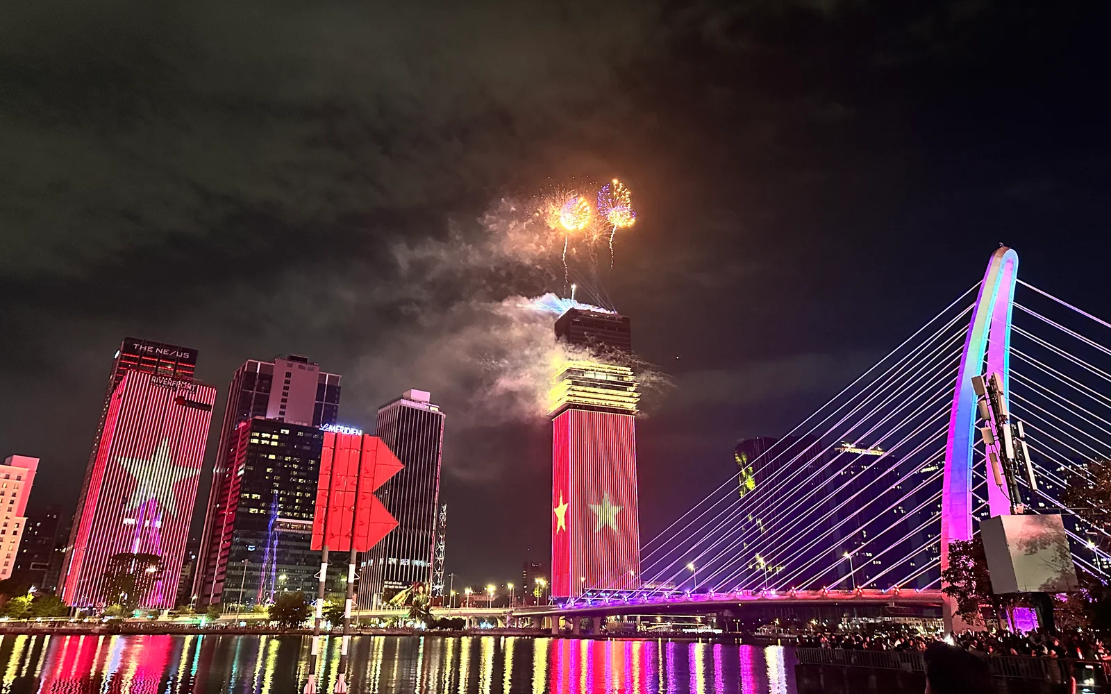Saigon waterfront at night — Vietnamese flag projected on the Bitexco tower, fireworks over Thủ Thiêm