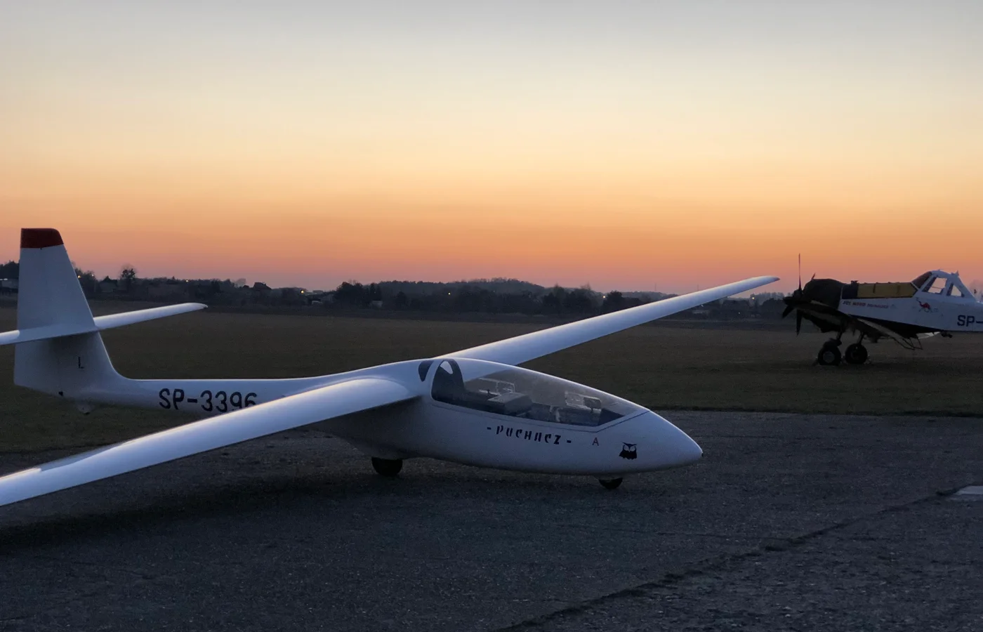 Dusk on the EPRG strip — a glider parked on the tarmac, low sun, the kind of light that doesn't survive in a photo.