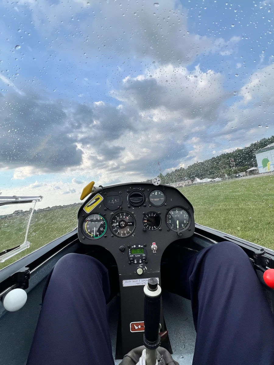 SZD Junior cockpit interior — instrument panel, legs forward, raindrops on the canopy.